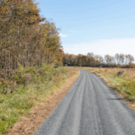 wąska droga gruntowa przecinająca zielone pole do samotnego domu w oddali